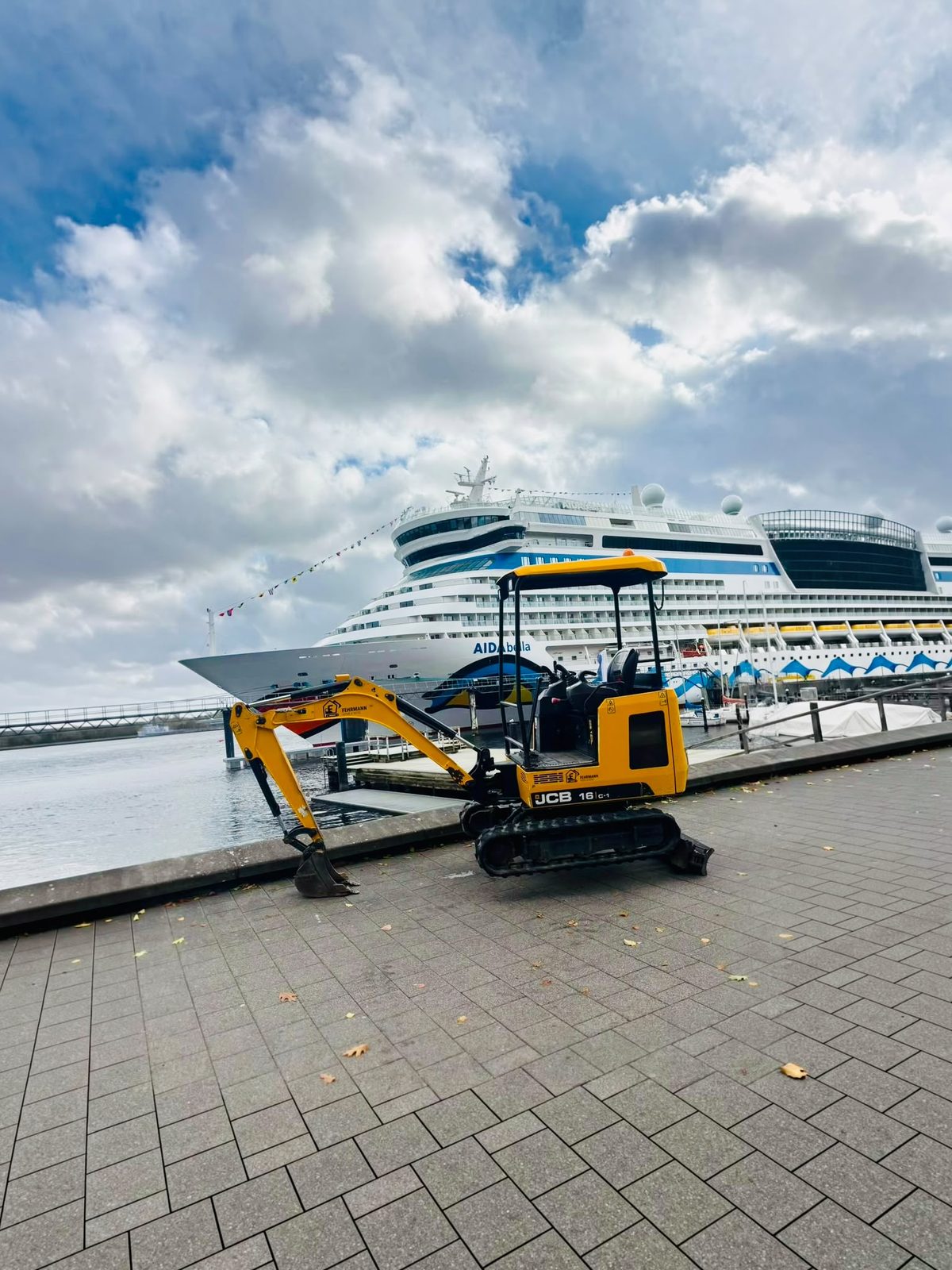 Minibagger JCB 16C-1 von Fehrmann Home & More an der Kieler Förde vor dem Kreuzfahrtschiff AIDAbella