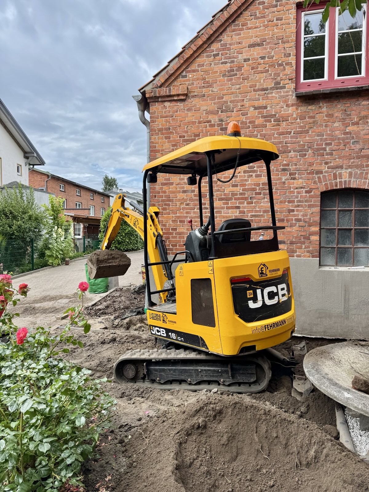 JCB 16C-1 bei Gartenarbeiten direkt am Wohnhaus zwischen Rosenbeeten