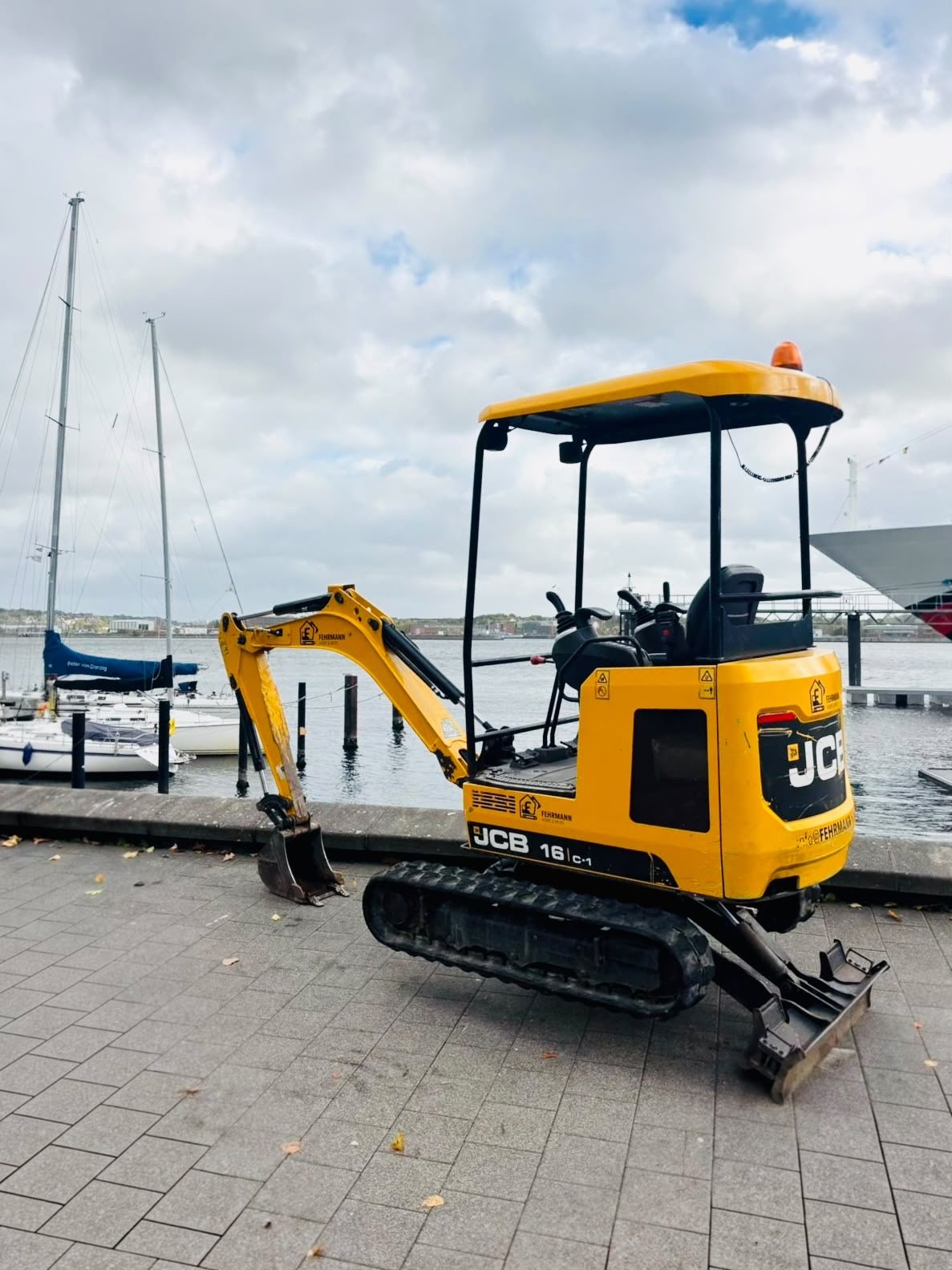 Minibagger JCB 16C-1 von Fehrmann Home & More an der Kieler Förde vor Segelbooten
